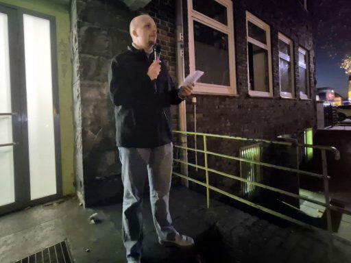 Mann mit Mikrofon spricht vor einem Gebäude in der Nacht.