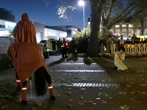 Eine Person in rotem Umhang steht auf einem Pferd, während eine andere Person kniet.