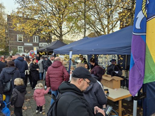 Belebte Veranstaltung mit Ständen und Besuchern unter Bäumen im Herbst.