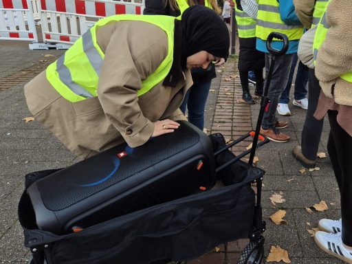 Person in gelber Warnweste beugt sich über einen Köfferchenwagen.
