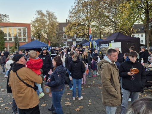 Menschenmenge auf einem Fest mit Ständen und Bäumen im Hintergrund. Herbstliche Atmosphäre.