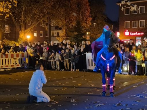 Eine Person kniet vor einem beleuchteten Pferd mit Reiter inmitten einer Menschenmenge bei Nacht.