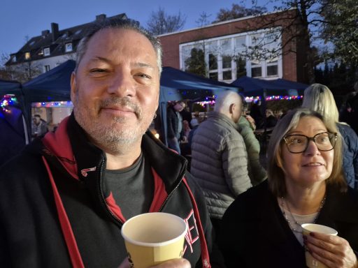 Zwei Personen mit Getränken stehen in einer Menschenmenge bei einer Veranstaltung.