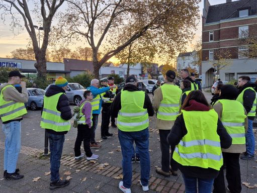 Gruppe von Menschen in leuchtenden Warnwesten versammelt sich bei Sonnenuntergang.