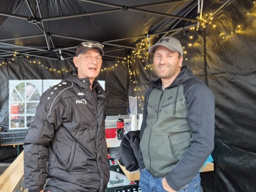 Zwei Männer stehen in einem Zelt mit Lichtern, lächeln und sprechen miteinander.