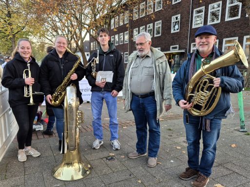 Fünf Musiker mit Blechblasinstrumenten stehen fröhlich auf einer Straße.